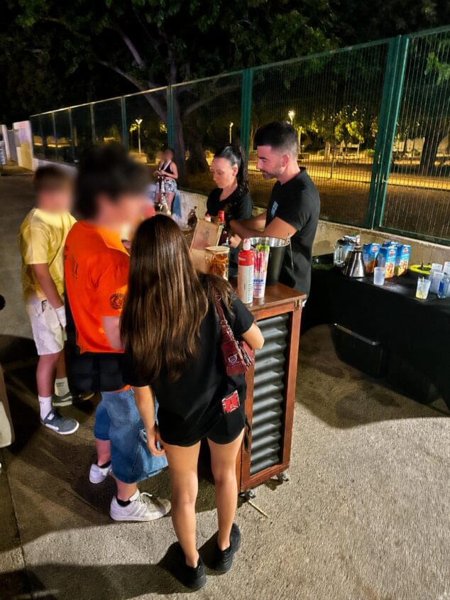Casi 500 jóvenes participan en Dénia en una campaña para prevenir el consumo de alcohol y drogas 3 Imagen: Personal de la campaña preventiva sirve cócteles sin alcohol a jóvenes en un stand nocturno durante la Fiesta Mayor de Dénia.
