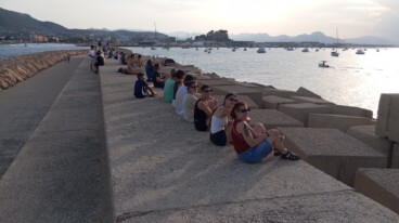 Personas esperando en las escolleras del puerto, con el Castell de Dénia al fondo y las gafas puestas