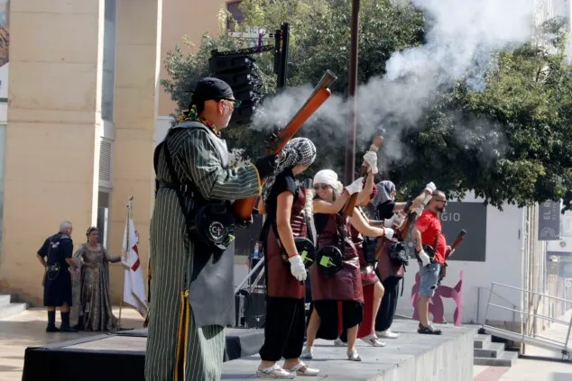 El atronador estallido de los arcabuces toma el centro de Dénia antes del esperado Milagro de la Niebla 2 Imagen: Representantes de las filaes moras y cristianas se alinean en la plaça del Consell de Dénia para la tradicional batalla de arcabucería
