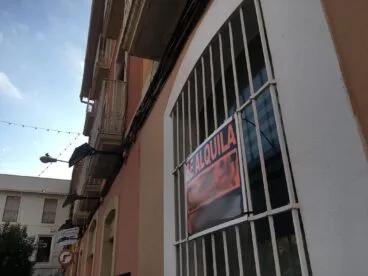 La Generalitat lanza el Bono Alquiler Joven 2026 de 250 euros al mes para alquilar en la Comunitat Valenciana 2 Fotografía de la fachada de un edificio con un gran cartel naranja y negro de 'SE ALQUILA' colgado en las rejas de una ventana o balcón.