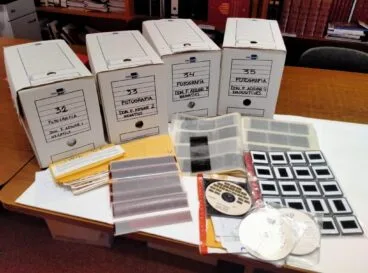 Más de 50.000 imágenes de la vida cotidiana de Dénia donadas por el fotógrafo Paco Adsuar 2 Cuatro cajas de archivo etiquetadas, tiras de negativos, diapositivas en fundas y CD sobre una mesa, parte de la donación de Paco Adsuar al Archivo de Dénia.