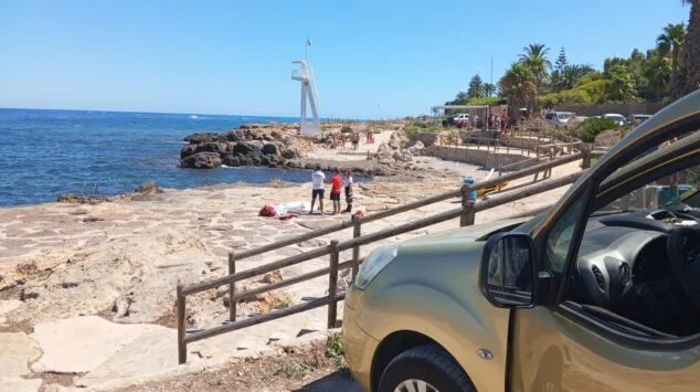 Fallece un hombre de 70 años tras sufrir un golpe en la cabeza en una playa de Dénia 2 Imagen: Personal de emergencias junto a una persona fallecida cubierta con una sábana en una zona rocosa costera.