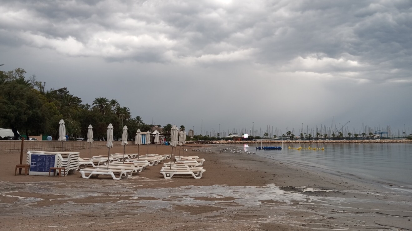 La playa vacía y con las sombrillas cerradas ante la llegada de la lluvia torrencial