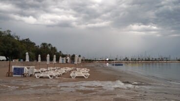 La playa vacía y con las sombrillas cerradas ante la llegada de la lluvia torrencial