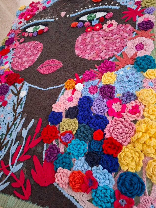 Obra de arte textil de Marita A. Guardia que representa el perfil de una mujer con un pelo hecho de coloridas flores de ganchillo.