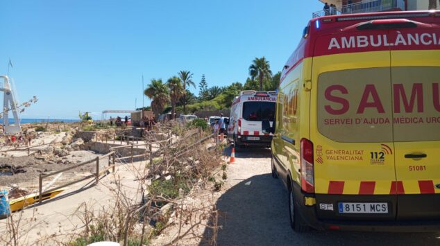 Fallece un hombre de 70 años tras sufrir un golpe en la cabeza en una playa de Dénia 4 Ambulancia amarilla del SAMU y helicóptero medicalizado estacionados en un área de tierra con vegetación cerca del mar.