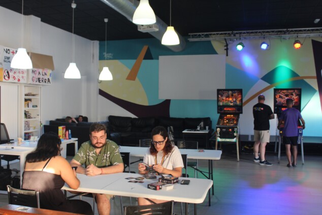 De la tirolina al rap sin alcohol: así vivieron los jóvenes de Dénia su día más intenso 2 Imagen: Partida de cartas en primer plano mientras, al fondo, otros jóvenes disfrutan de las máquinas arcade