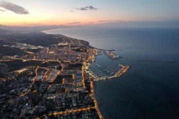 Dénia supera la media de más de 250 destinos en su camino para convertirse en Destino Turístico Inteligente 3 Vista aérea del puerto y la ciudad de Dénia al atardecer con las luces urbanas encendidas.