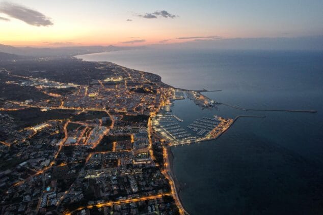 Vista aérea del puerto y la ciudad de Dénia al atardecer con las luces urbanas encendidas.