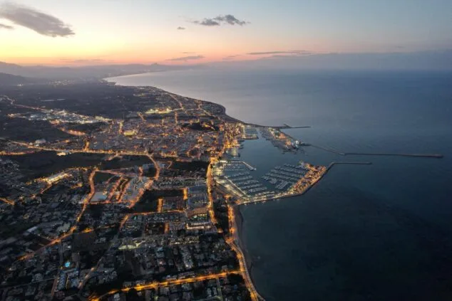 Vista aérea del puerto y la ciudad de Dénia al atardecer con las luces urbanas encendidas.