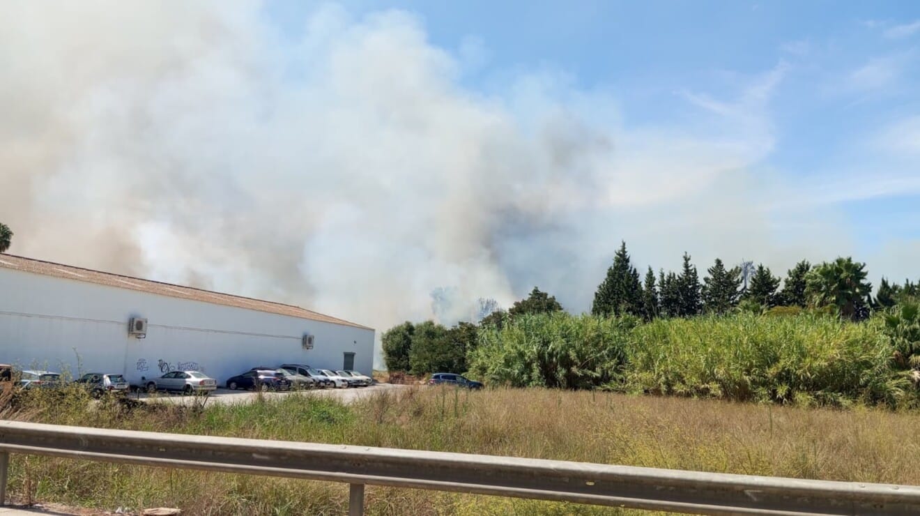 El humo se eleva tras la nave industrial, alimentado por la maleza seca cercana