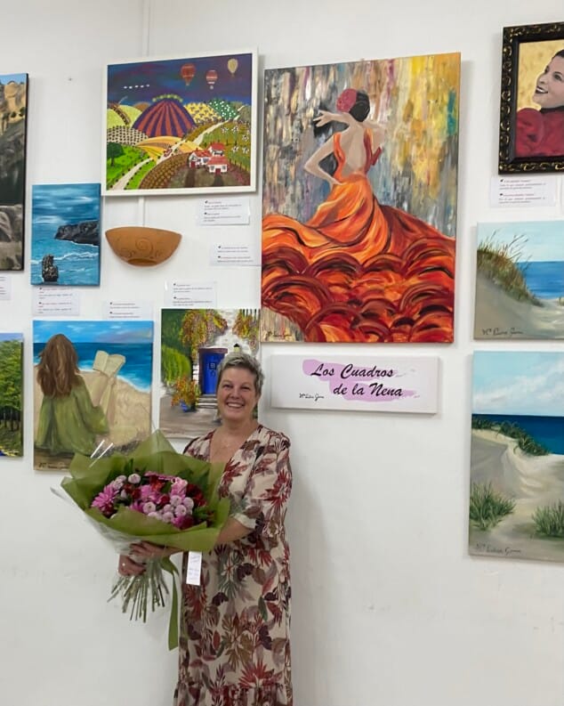 Imagen: María Luisa Gema Bisquert posa con un ramo de flores delante de varias de sus pinturas.