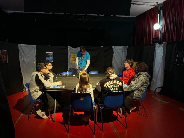 Imagen: Varios jóvenes sentados alrededor de una mesa jugando a un juego de tablero en un espacio interior.