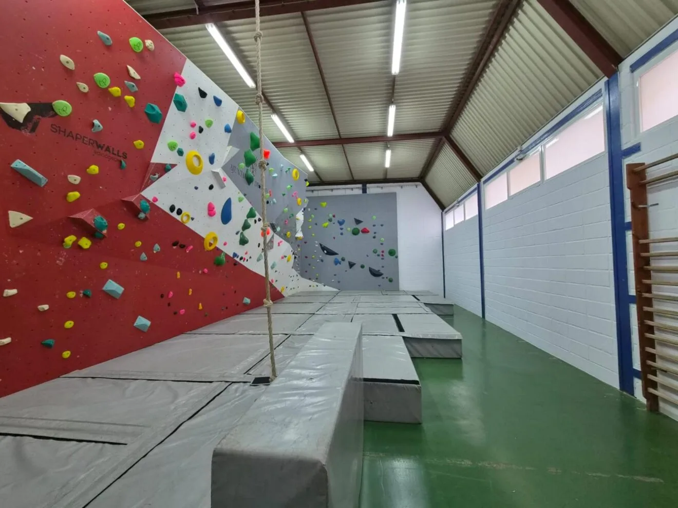 Photographie de l'intérieur du nouveau mur d'escalade municipal de Dénia, montrant des murs d'escalade avec des prises colorées et des tapis au sol.