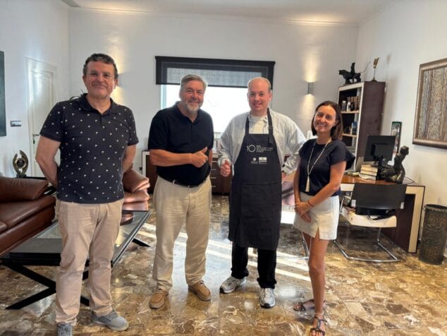 Dénia, referente europeo: un experto alemán estudia sus mercados y gastronomía 2 Imagen: Foto de grupo con cuatro personas en una oficina: el alcalde de Dénia, un concejal, el técnico alemán Daniel Schellwald con un delantal y una representante municipal, durante una recepción.