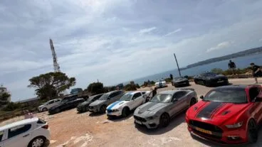 Varios coches Ford Mustang aparcados en una concentración en un terreno de tierra cerca del mar