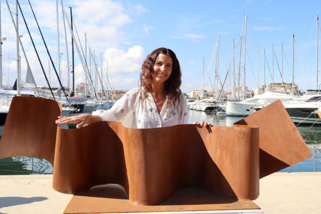«Save the ocean» de Mapi Gómez, gana el primer premio de la 8ª edición de 'Esculturas frente al mar' de Dénia 2 Imagen: Mapi Gómez sonríe junto a su escultura de metal oxidado "Save the ocean" en un puerto deportivo.