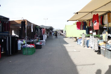 Carlos Barona (PP) alerta del «caos» de tráfico en Dénia y propone cambios para los viernes de mercadillo 5 Mercadillo ambulante en Dénia con puestos de ropa instalados a ambos lados de una calle y personas caminando entre ellos.