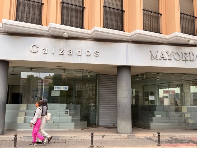 Luces apagadas y un escaparate desierto: el adiós a la mítica esquina de Calzados Mayordomo en Dénia 2 Imagen: Peatones paseando junto al escaparate del local, donde aún cuelgan los carteles del remate final