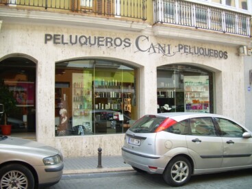 Fachada de Cani Peluqueros en Dénia, con varios coches estacionados frente al establecimiento antes de la peatonalización de la calle.