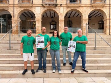 Dénia vivirá un domingo histórico con la I Diada de la Muixeranga de la Marina Alta 1 Cinco miembros de la Muixeranga de la Marina Alta con camisetas verdes sostienen carteles de la "I Diada" en unas escaleras de piedra.