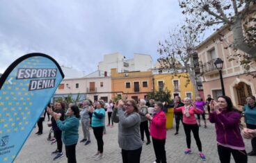 Grupo de personas haciendo ejercicio en una plaza pública con una pancarta de Esports Dénia al fondo.